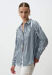 Gestreepte blouse met verticale marineblauwe en lichtblauwe strepen, een gekraagde halslijn, knoopsluiting aan de voorkant en lange mouwen met knoopmanchetten.