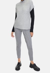 Šedý pletený svetr s texturou a vysokým límcem, doplněný úzkými šedými tepláky a černými platformovými botami na šněrování.