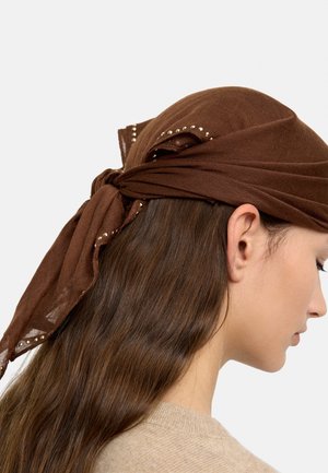 Kobieta z długimi brązowymi włosami, nosząca brązową chustkę na głowie, zawiązaną z tyłu, ozdobioną małymi metalowymi ćwiekami wzdłuż krawędzi.
