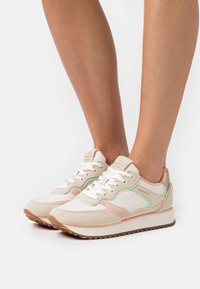 Shoe, primarily white with pink and mint accents, features a suede and mesh design, rounded shape, and textured rubber sole.