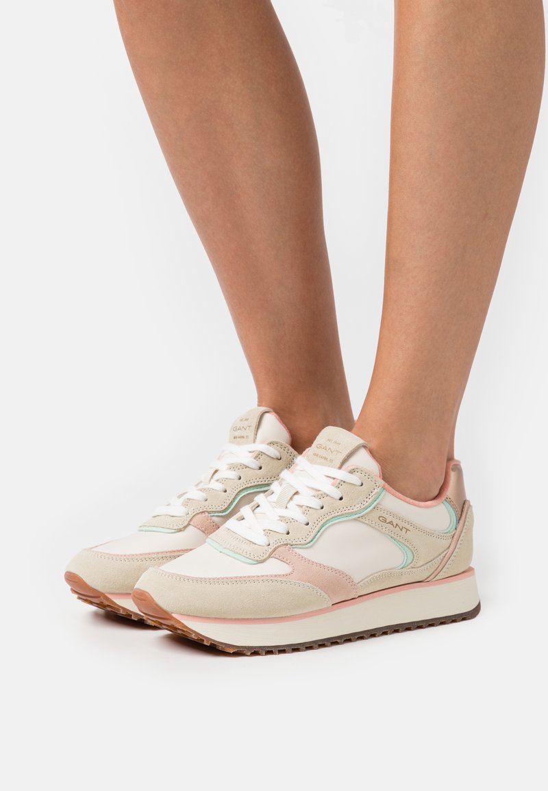 Shoe, primarily white with pink and mint accents, features a suede and mesh design, rounded shape, and textured rubber sole.