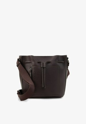 Donkerbruine, getextureerde leren bucketbag met verstelbare brede stoffen schouderriem en voorvak met rits op een witte achtergrond.