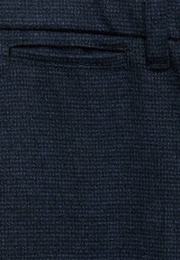 Pantaloni textured blu scuro con un leggero motivo a scacchi. Presentano una singola tasca frontale e passanti per cintura. Il tessuto appare tessuto e durevole.
