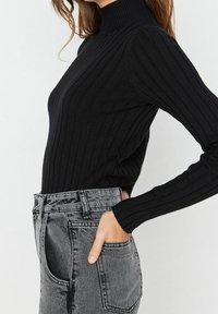 Schwarzer gerippter Rollkragenpullover mit langen Ärmeln, kombiniert mit hoch taillierten grauen Jeans aus Denim mit Seitentaschen und einem lockeren Schnitt.