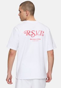 Hvid bomulds t-shirt med korte ærmer, der har et rødt logo "R.S.V.P." og tekst på ryggen, rund halsudskæring og afslappet pasform.
