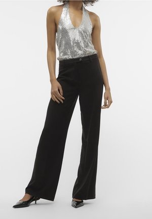 Sølv paliettop med halterneck og sorte bukser med vide ben, kombineret med sorte spidse hæle. Outfittet har en slank, moderne silhuet.