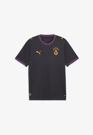 Camiseta deportiva gris oscuro con cuello y bordes de las mangas morados, logos naranjas de Puma y un escudo naranja del equipo Galatasaray con cinco estrellas.