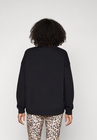 Zwarte sweatshirt met een ronde halslijn en verlaagde schouders, gecombineerd met legging in luipaardprint met een zachte, rekbare textuur.