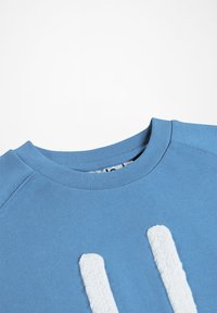 Sudadera azul con cuello redondo, que presenta un detalle gráfico blanco suave y texturizado en el frente. Fabricada en tejido de jersey con puños de canalé.