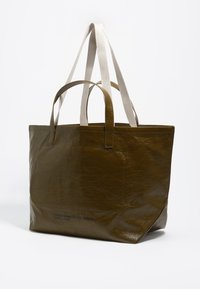 Olive zelena, sijoča torba iz sintetičnega materiala, z dvojno tkaninasto ročajem in besedilnim detajlom na eni strani. Pravokotna oblika.