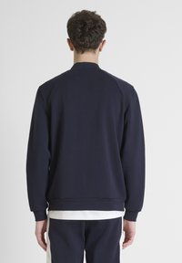 Felpa navy con scollatura a girocollo classica, maniche lunghe e polsini a coste. Il tessuto appare morbido e confortevole, con un design semplice.