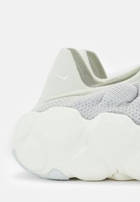 Világosszürke kötött sneaker texturált felsőrésszel, sima fehér talppal és kis Nike logóval a sarkán. Lekerekített, formázott dizájnnal rendelkezik.