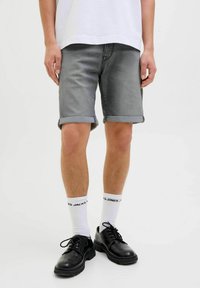 Grijze denim shorts met opgerolde zomen, gedragen met witte sokken en zwarte schoenen. De stof heeft een gladde textuur en een subtiele wassing.