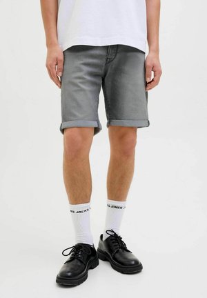 Grå denimshorts med uppvikta ben, bärs med vita strumpor och svarta skor. Tyget har en slät textur och en subtil tvätteffekt.
