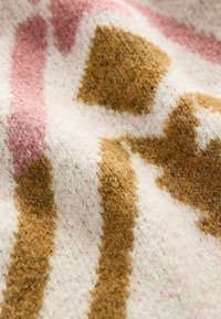 Tissu tricoté doux avec des formes géométriques marron et roses texturées sur un fond crème, présentant un gros plan du motif tissé.