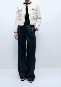 Biała teksturowana kurtka z różowym wykończeniem, z zapięciem na guziki i kieszeniami naszytymi. Połączona z szerokimi spodniami skórzanymi w kolorze czarnym i butami z odkrytymi palcami.