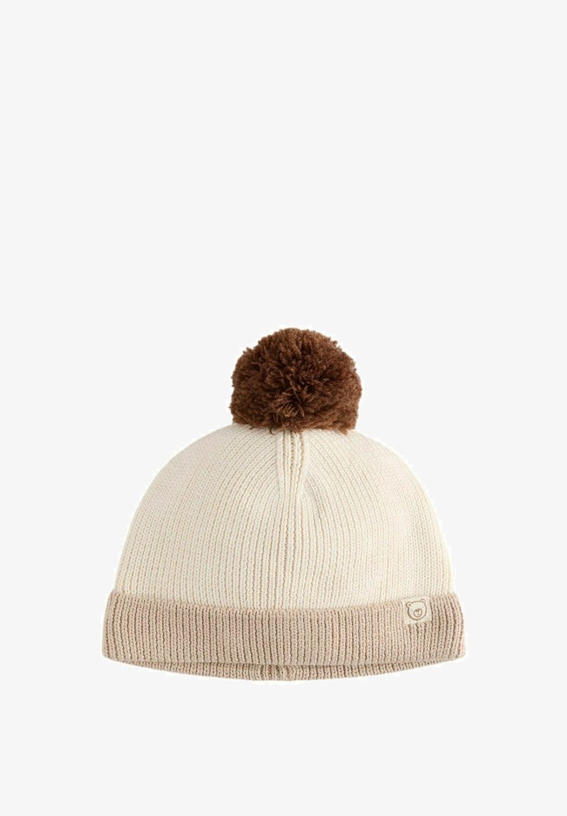 Gehaakte beanie in crème met een bruine pompon bovenop, met een geribbeld textuur en een opgevouwen beige manchet met een klein logo-label.