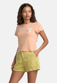 Kortærmet koral-lyserød bomulds t-shirt med et blomsterdesign i hvid og grøn. Parret med teksturerede, lysegrønne kordfløjlshorts.