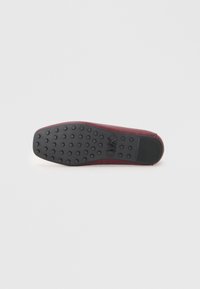 Scarpa piatta bordeaux con materiale liscio, dotata di una suola in gomma nera testurizzata con impugnature circolari e un sottile dettaglio del logo sul lato.