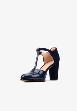 Granatowe buty na wysokim obcasie z paskiem w kształcie litery T, zamkniętym zaokrąglonym noskiem, fakturowaną skórzaną przednią częścią oraz materiałem zamszowym na pięcie i pasku wokół kostki.