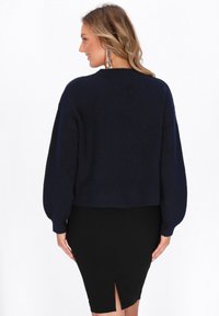 Marineblauwe cropped trui met lange, volumineuze mouwen en een zachte textuur, gecombineerd met een aansluitende zwarte kokerrok met een split.