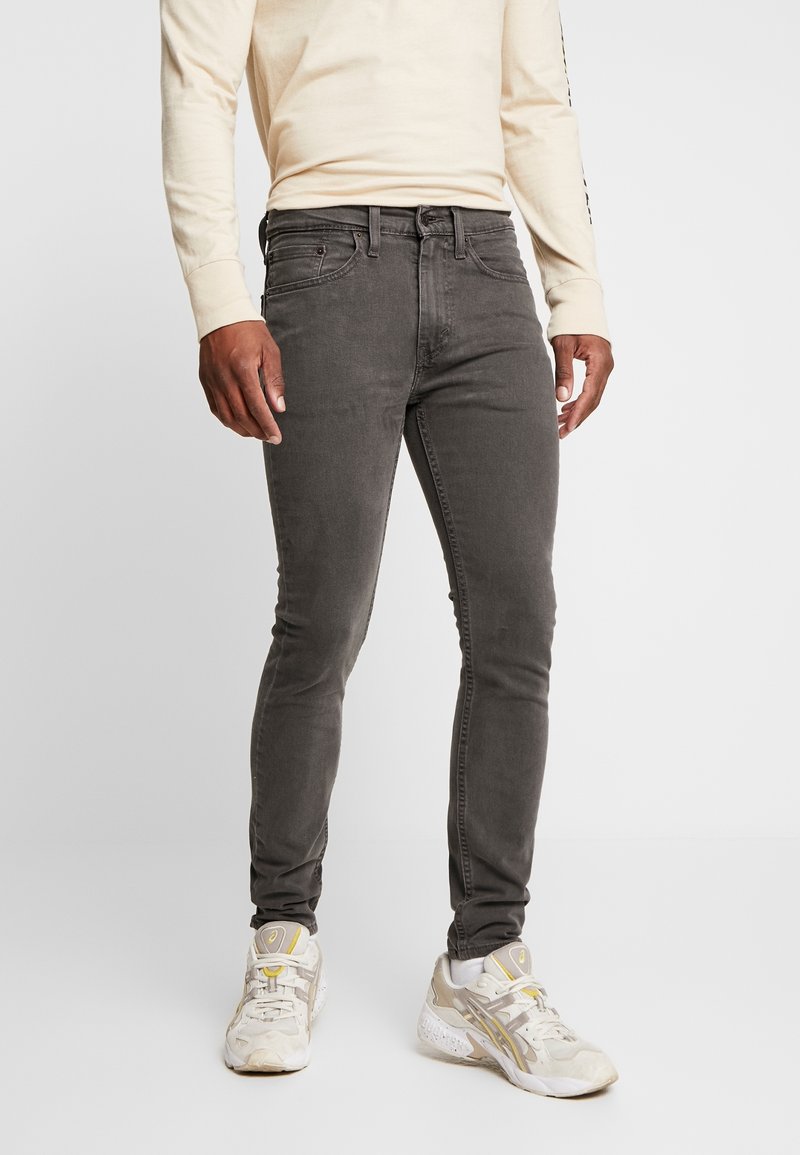 Jeans ajustados grises con una textura suave, diseño de cinco bolsillos y cierre de botón, combinados con una camisa de manga larga beige y zapatillas ligeras.
