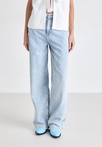 Lys blå denim vide bukser med en slidt finish, med klassisk fem-lomme design og en afslappet pasform. Kombineret med blå fodtøj.