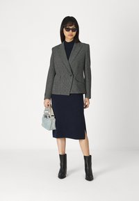 Blazer grigio a tartan con spalle strutturate, abito blu navy con spacco laterale, stivali neri fino al ginocchio e borsa azzurro chiaro.