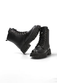 Botas de tobillo de cuero negro con un diseño de cordones, punta redonda y suela de goma texturizada y gruesa. Presenta ojales de metal y un cuello acolchado.