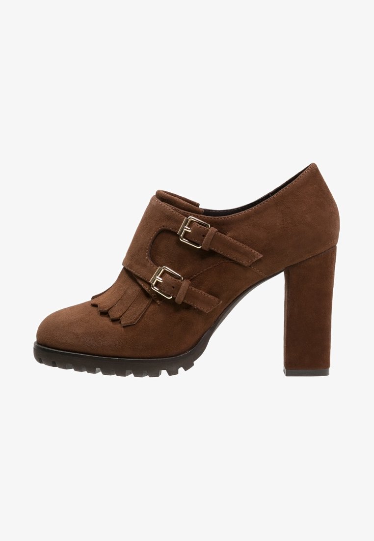 Bruna mockaskor med hög klack, två justerbara spännen, fransdetaljer fram och en tjock strukturerad sula.