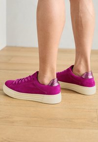 Sneaker in camoscio fucsia con un accento in oro rosa sul tallone e suola in gomma beige, presentano lacci piatti e un design con punta arrotondata.