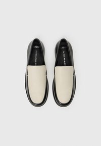 Μαύρα και κρεμ παντόφλες με γυαλιστερό δέρμα, στρογγυλή φόρμα, μινιμαλιστικό σχέδιο και χωρίς ορατές εφαρμογές ή σχέδια.
