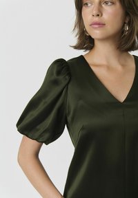 Rochie de satin cu mâneci bufante, de culoare verde închis, cu decolteu în V și textură netedă. Prezintă cusături minime și o siluetă ajustată.