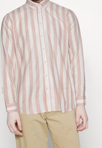 Linneknäppt skjorta med vertikala rosa och vita ränder, långa ärmar och klassisk krage. Framsidan har knäppning och detaljer vid manschetterna.