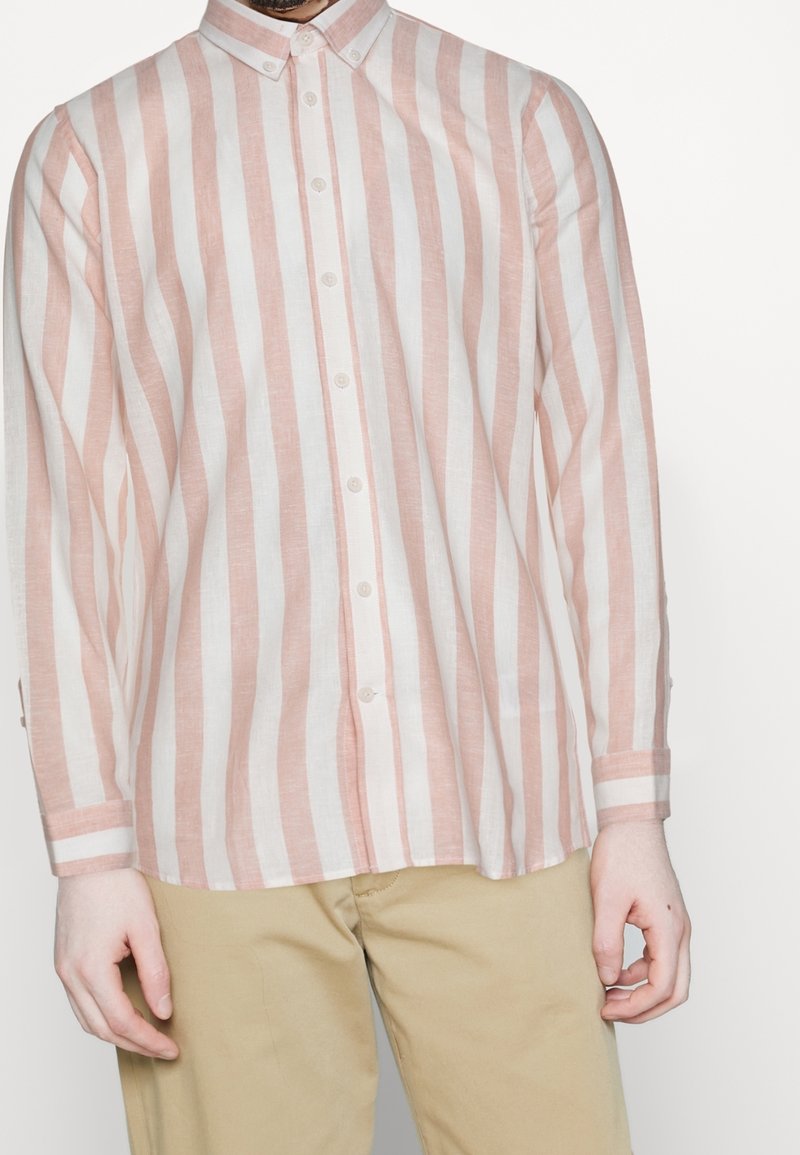 Linneknäppt skjorta med vertikala rosa och vita ränder, långa ärmar och klassisk krage. Framsidan har knäppning och detaljer vid manschetterna.