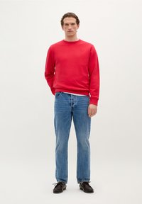 Rød sweatshirt med rund hals, ribbede manchetter og talje, parret med lyseblå lige ben jeans og sorte sko. Enkel design, ensfarvede farver.