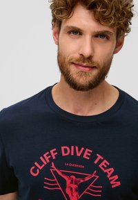 Námořnické bavlněné tričko s červenou grafikou potápěče a textem "CLIFF DIVE TEAM LA QUEBRADA" v kruhovém uspořádání. Měkká textura, kulatý výstřih.