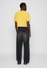 Gul crop t-skjorte med korte ermer, kombinert med høyt liv, mørkegrå vide jeans med baklommer og logo.