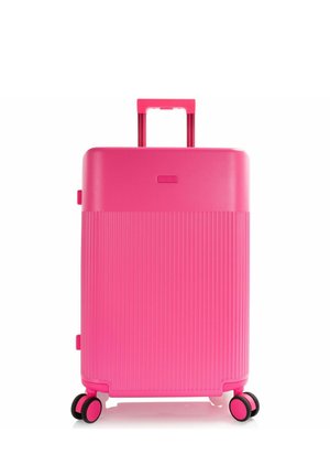 Valigia rigida rosa acceso con metà inferiore costolata, manico telescopico esteso e quattro ruote doppie girevoli.