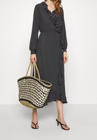 Svart klänning med prickar, rynkad krage och ärmar, midjan åtdragen och knäppning framtill. Vevad halmbyxa med krämfärgad mönstring och dubbla handtag.