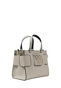 Borsa a tracolla sintetica beige con un design strutturato, caratterizzata da un grande logo frontale e dettagli neri a contrasto. Doppi manici corti e fiocchi laterali.