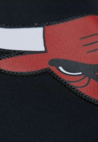 Schwarzer Stoff mit einer roten Cartoon-Wolf-Illustration, der weiße Zähne und schwarze Schnurrhaare zeigt, mit deutlich sichtbarem Stich entlang der Kanten.