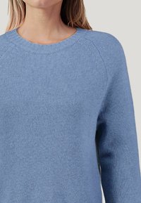 Helles blaues Strickpullover aus weichem Material; runder Halsausschnitt, lange Raglanärmel und mit strukturiertem Finish.