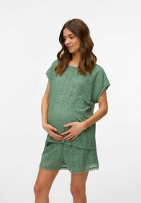 Conjunto de maternidad verde de encaje que incluye una blusa suelta con mangas cortas y pantalones cortos a juego, ambos adornados con un patrón circular y bordes con forma de onda.