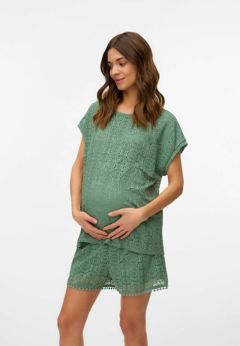 Conjunto de maternidad verde de encaje que incluye una blusa suelta con mangas cortas y pantalones cortos a juego, ambos adornados con un patrón circular y bordes con forma de onda.