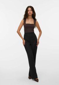 Top sans manches marron avec un encolure carrée associé à un pantalon noir taille haute. Le modèle porte des chaussures pointed marron. Design simple et ajusté.