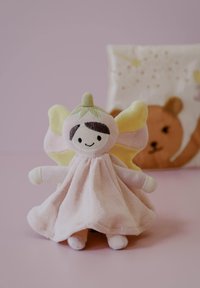 Minkšta lėlė iš audinio su rožinės spalvos kūnu, geltonais sparnais ir žalią karūną. Ant veido išsiuvinėti bruožai, o tekstūra – ką tik užuolaidinio audinio.