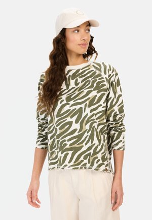 Green and cream long-sleeve shirt with a wavy camouflage pattern, soft material, and a rounded neckline. Paired with light-colored trousers.