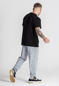 Čierne bavlnené tričko, voľný strih. Tmavo šedé tepláky s čiernym textom, elastický pás. Čierne tenisky s bielymi podrážkami a doplnkami.