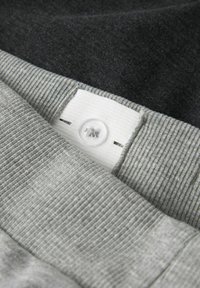 Prim-plan cu material din țesătură gri și neagră, cu dungi, cu un nasture alb cusut pe secțiunea gri, evidențiind textura textilă și detaliile cusăturii.